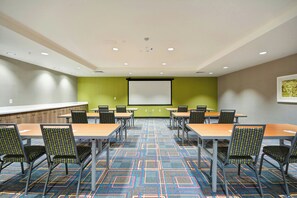 A conference room with a projector screen, multiple tables, chairs, and a patterned carpet. - Home2 Suites By Hilton Livermore (Livermore)