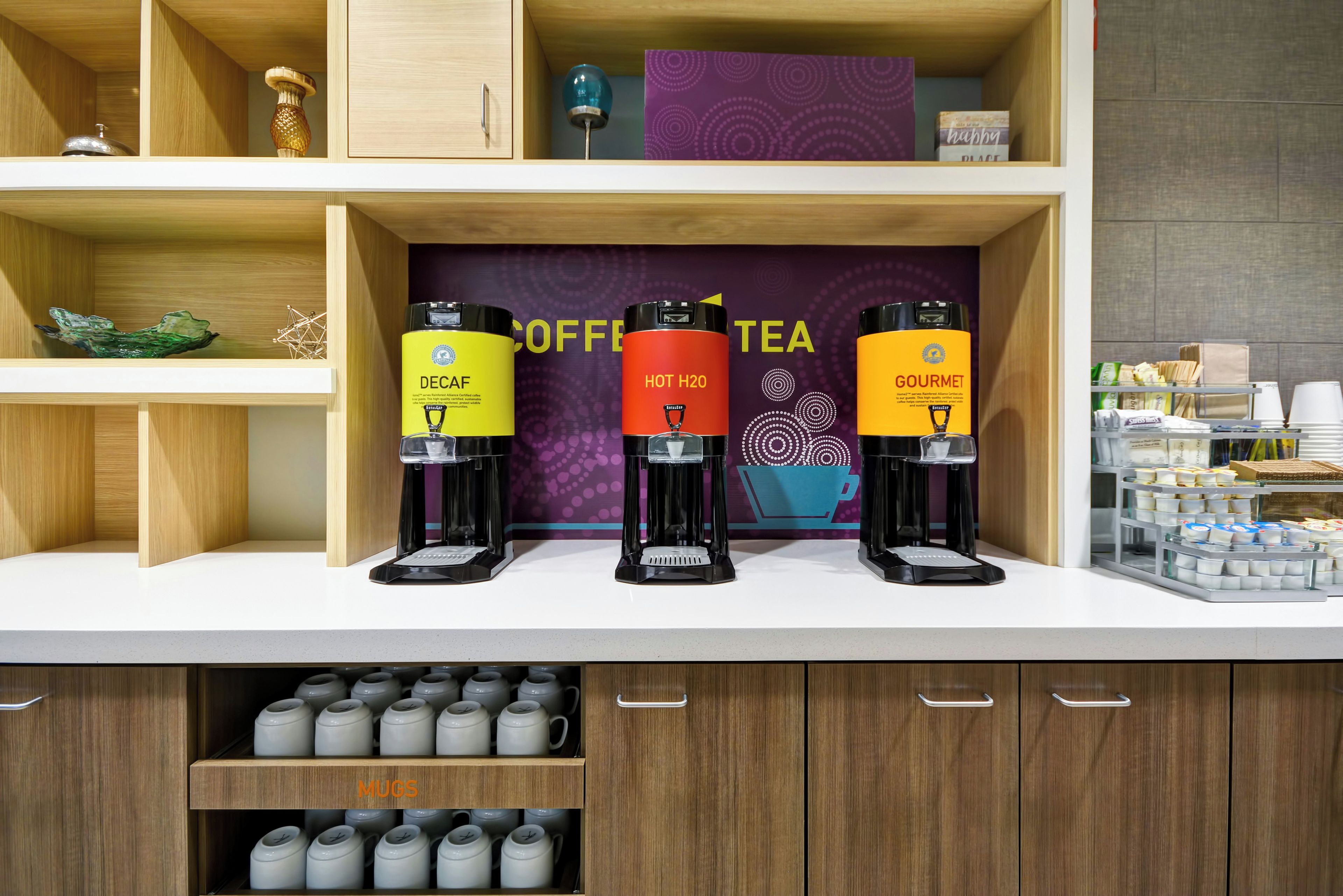 Estación de café y té con tres dispensadores etiquetados como Descafeinado, Agua Caliente y Gourmet.