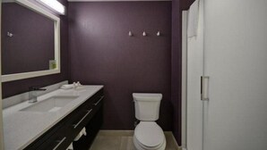 A bathroom with a white toilet, a vanity with a mirror, and a light fixture above the mirror. - Home2 Suites By Hilton Livermore (Livermore)
