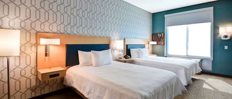 A hotel room with two beds, a patterned wall, a large window, and a nightstand with a lamp.
