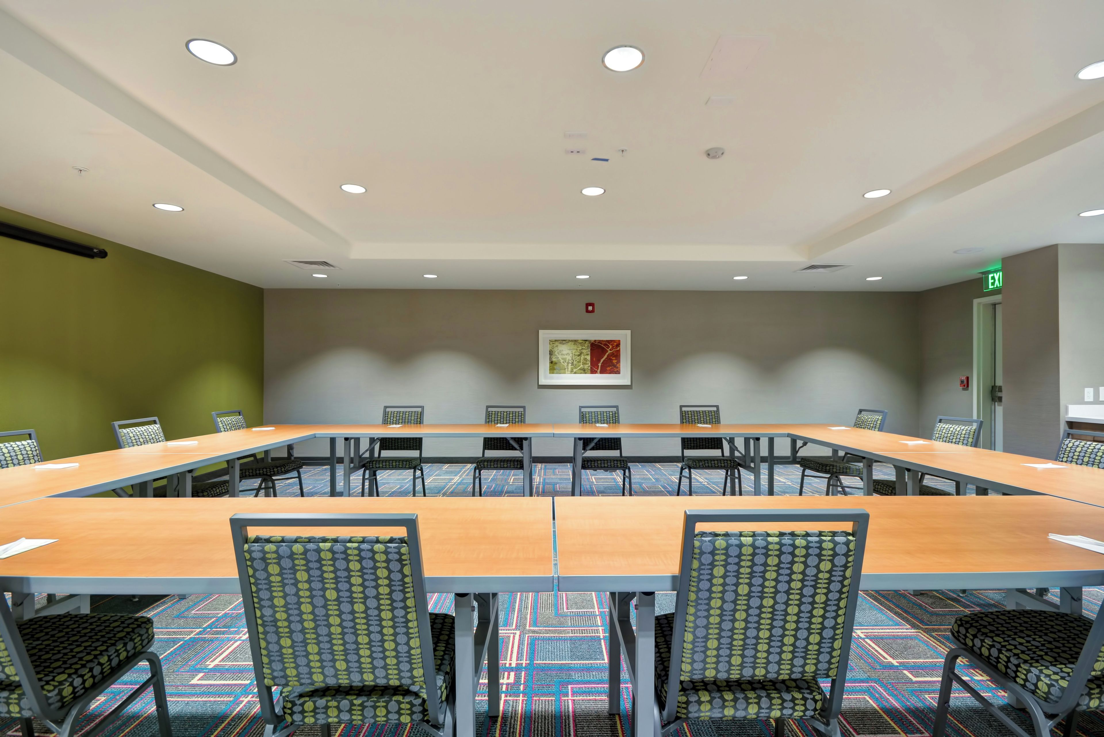 Une salle de conférence avec une longue table et des chaises, un détecteur d’incendie et un panneau indiquant la sortie.