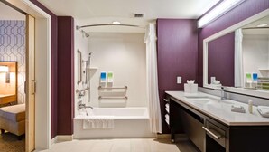 A modern bathroom with a bathtub, shower, and vanity with a large mirror. - Home2 Suites By Hilton Livermore (Livermore)