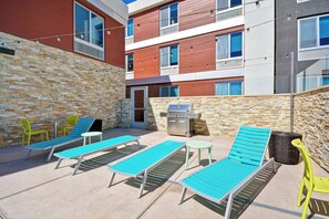 Un área de descanso al aire libre con varios sillones reclinables, una parrilla y una pared de piedra.