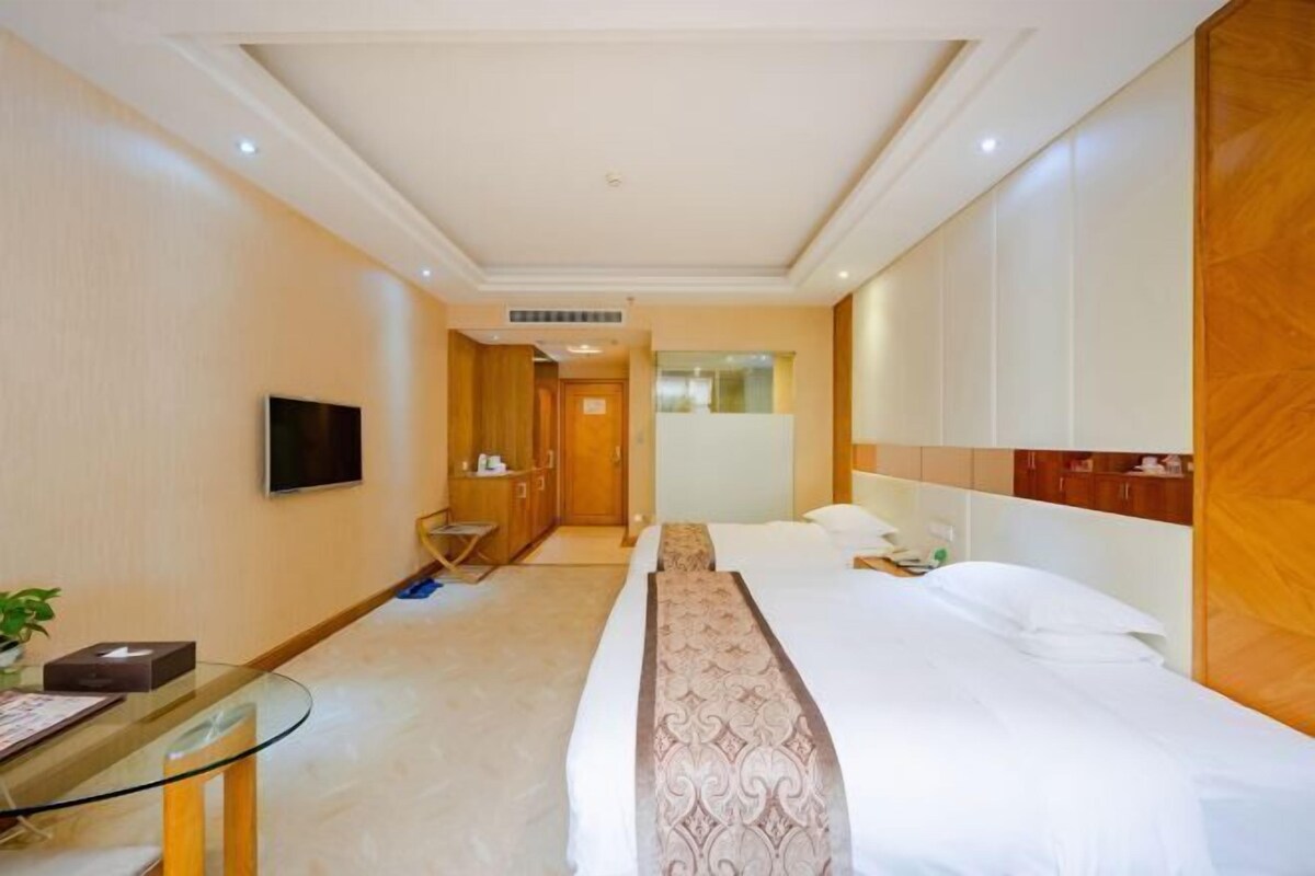 Una habitación de hotel con una cama, un televisor montado en la pared, una mesita de vidrio y un armario de madera.