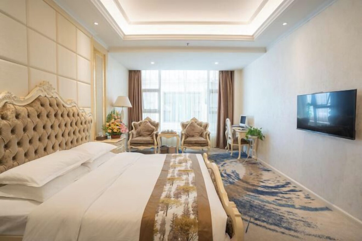 Habitación de hotel con una cama grande, un televisor montado en la pared y una zona de estar con dos sillones y una mesa.