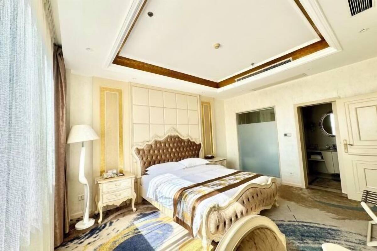 Un dormitorio con una cama grande, una mesita de noche, una lámpara y la puerta del baño.