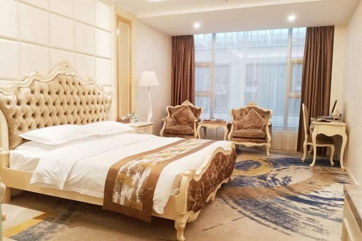 Habitación de hotel con una cama grande, dos sillones, una mesita y una ventana con cortinas.