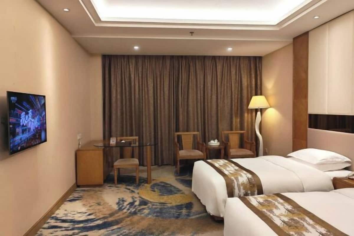Una habitación de hotel con dos camas, un televisor, un escritorio con sillas y una lámpara.