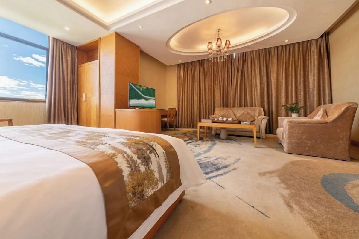 A hotel room with a large bed, a sofa, a coffee table, and a TV.