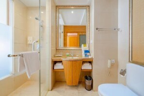 Un baño con cabina de ducha de vidrio, tocador de madera, inodoro blanco y espejo sobre el lavabo.
