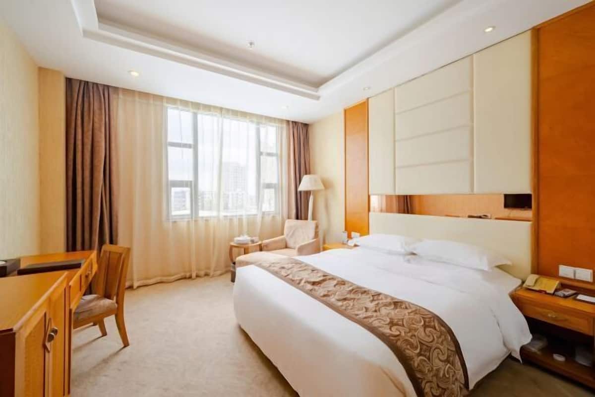 Una habitación de hotel con una cama grande, un escritorio, una silla y una mesita de noche.