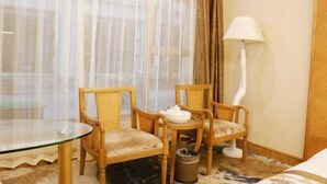 Una habitación de hotel con una mesa de vidrio, dos sillas de madera, una lámpara blanca y una cama.