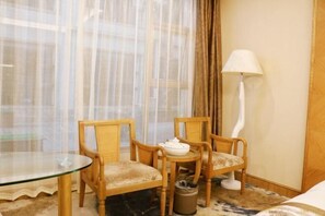 Una habitación de hotel con una mesa de vidrio, dos sillas de madera, una lámpara blanca y una cama.