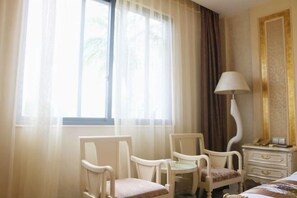 A hotel room with a bed, two chairs, a nightstand, a lamp, and a window with sheer curtains. - Island Hotel (Dongshan County)