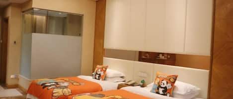 A hotel room with two beds, each with an orange bedspread featuring cartoon characters. There is a large mirror above the beds and a wooden headboard.