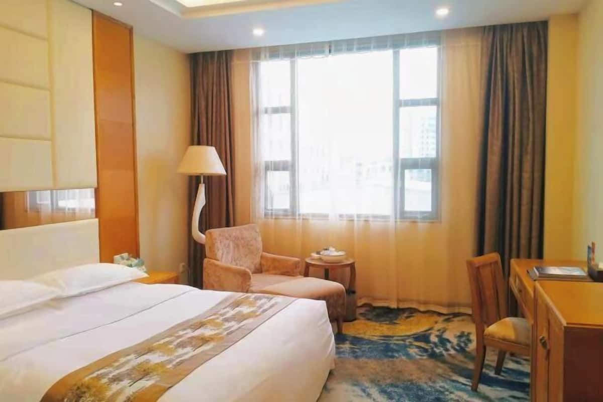 Una habitación de hotel con cama, una silla, un escritorio y una ventana con cortinas.