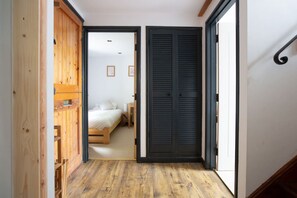A narrow hallway with wooden flooring leading to a bedroom with a bed and a nightstand.