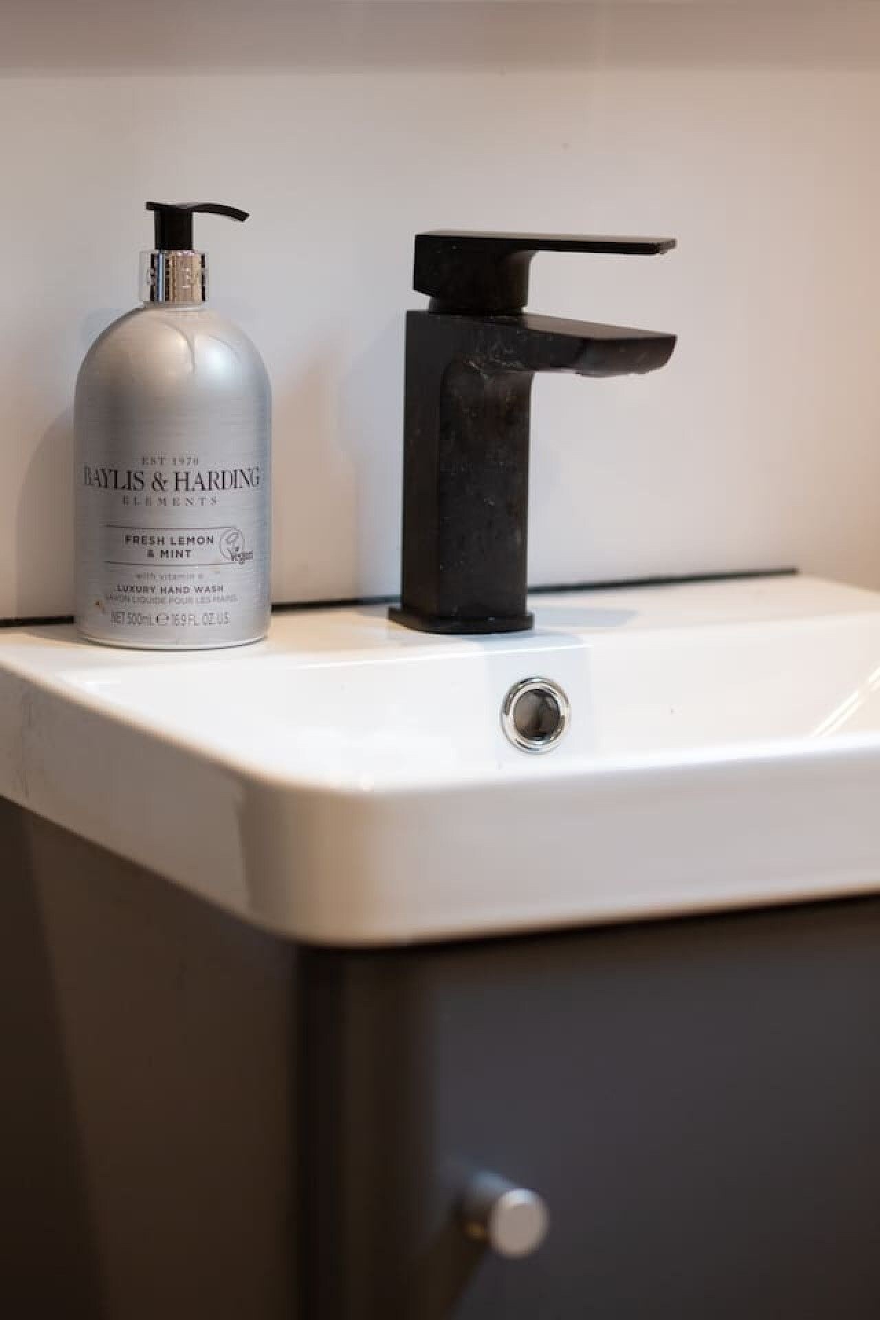 A bathroom sink with a bottle of Baylis & Harding Elements hand wash and a black faucet.