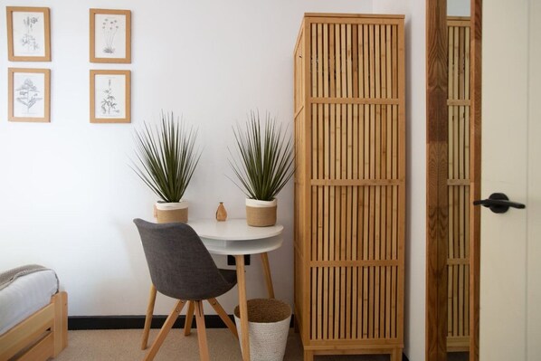 A room with a bed, a small table with two potted plants, a chair, and a wooden cabinet.