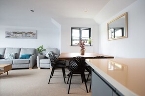 A modern living room with a sofa, dining table, chairs, and a kitchen area.