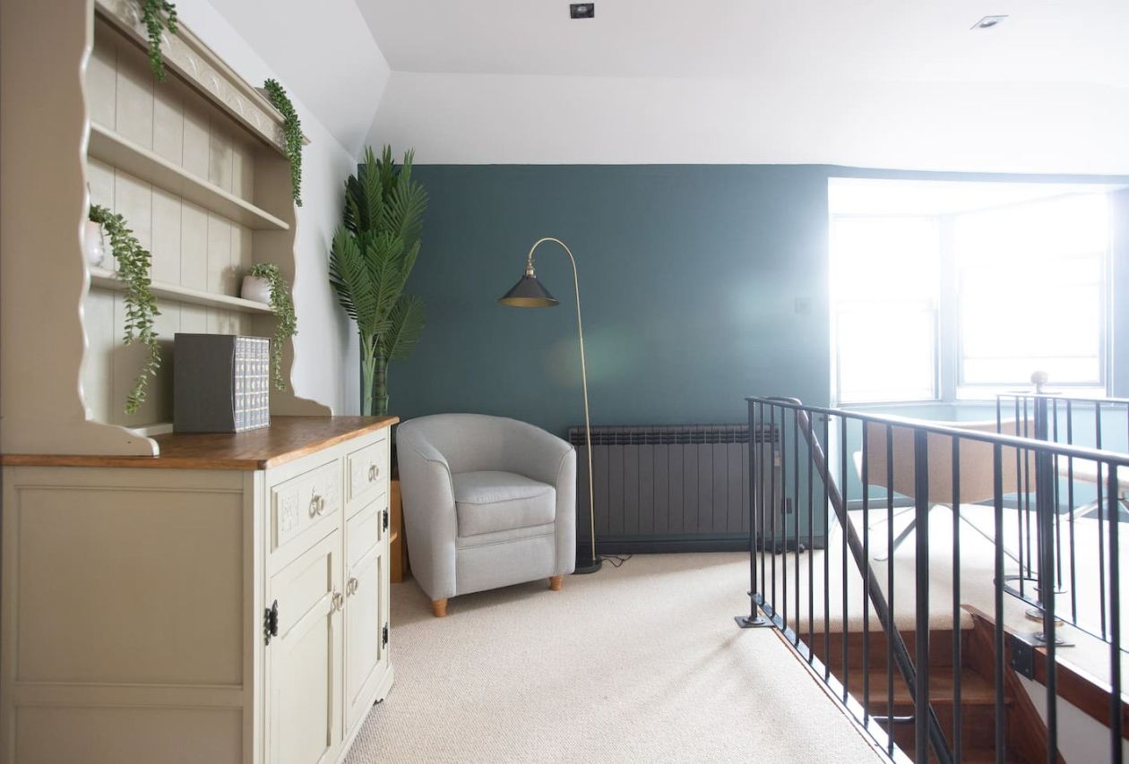 A room with a white dresser, a grey armchair, a floor lamp, and a view of a balcony.