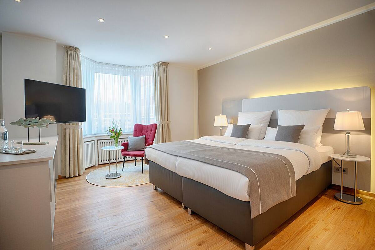A modern hotel room with a large bed, a flat-screen TV, a small table, and a red chair.