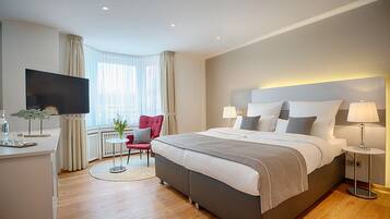 A modern hotel room with a large bed, a flat-screen TV, a small table, and a red chair.