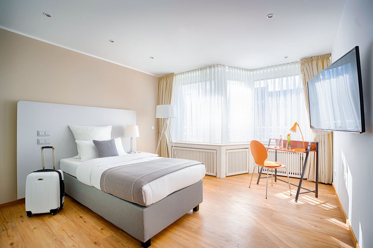 A hotel room with a bed, a desk, a chair, a TV, and a suitcase.