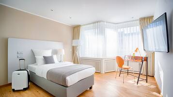 A hotel room with a bed, a desk, a chair, a TV, and a suitcase.