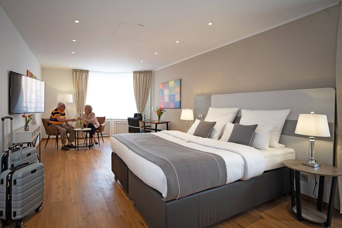 A modern hotel room with a large bed, bedside tables, a desk, and a seating area.