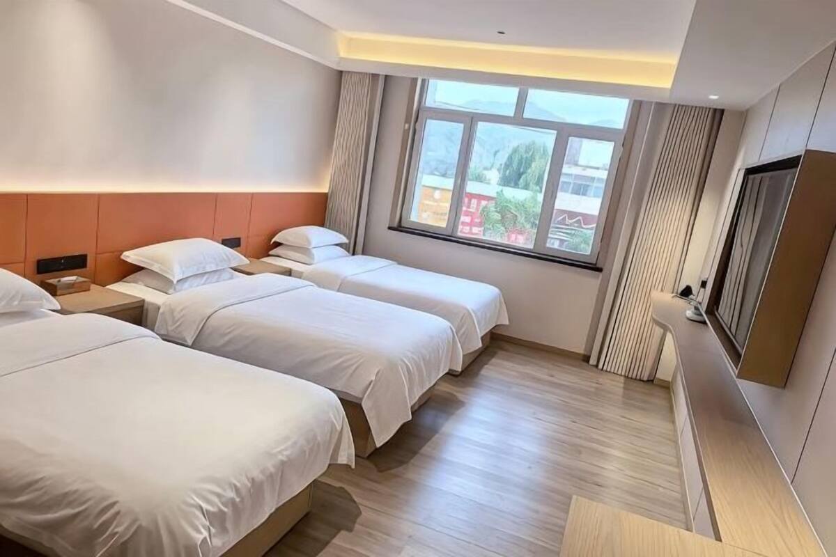 Habitación de hotel con tres camas, un televisor y un ventanal grande.