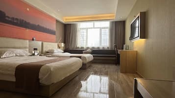 A hotel room with two beds, a large window, a painting on the wall, and a TV mounted on the wall.