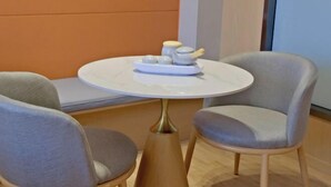 A round table with a white top and a gold base, surrounded by two grey upholstered chairs. - Captain Chain Hotel (Daixian Selected) (Dai County)