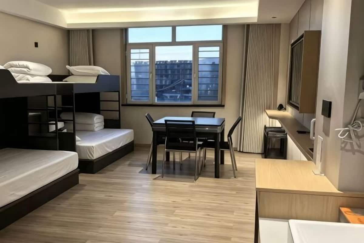 Una habitación con literas, un escritorio, sillas, un ventanal con vistas y una pequeña kitchenette.