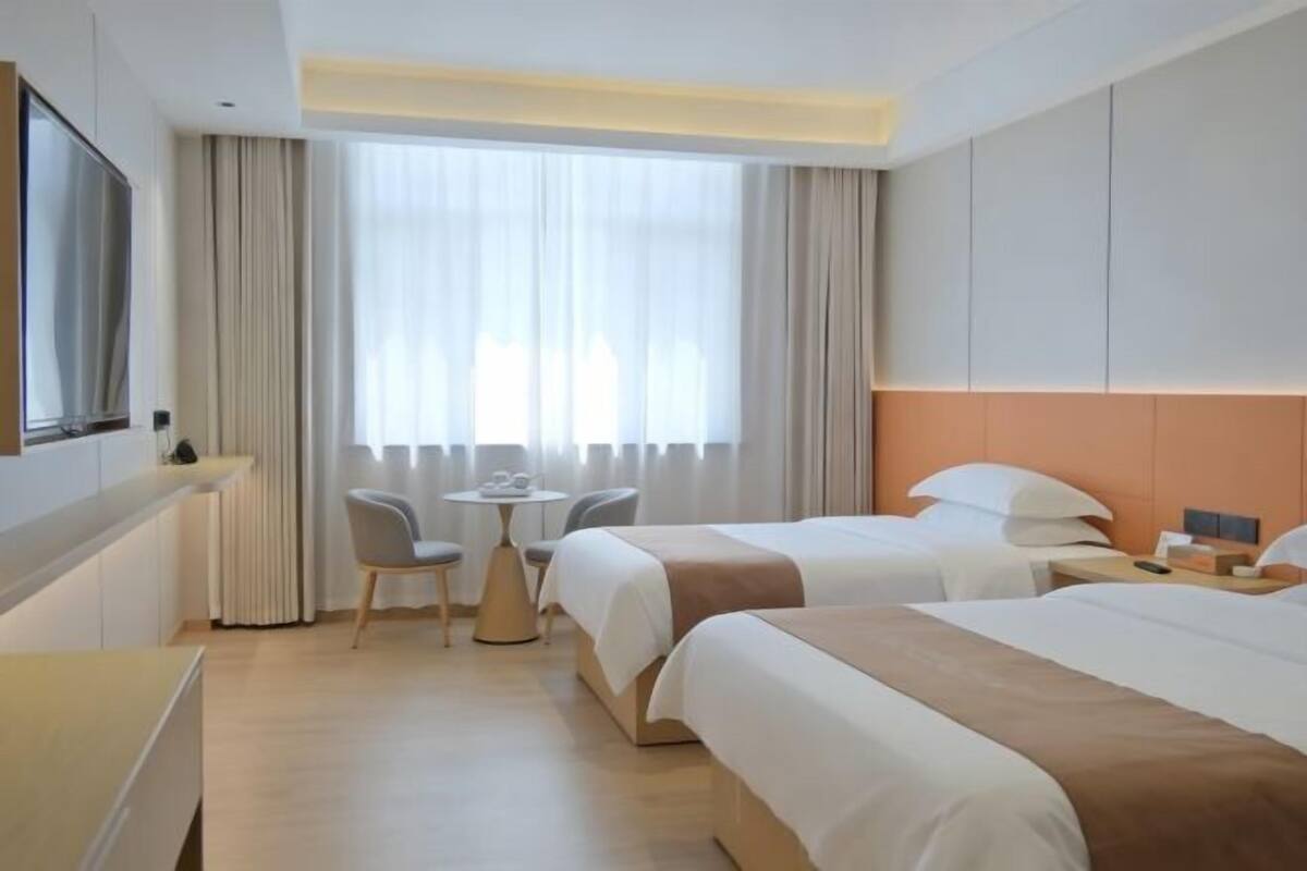 Habitación de hotel con dos camas, televisión, una mesita y ventana con cortinas.