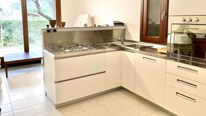 A modern kitchen with white cabinets, a stainless steel stove, and a large window with a view of greenery. - Holiday home mit Garten (Rosolina)