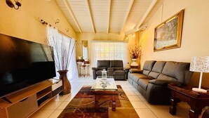 A living room with a flat-screen TV, a sofa, a coffee table, and a rug. - Donhenri House Hodges Bay in Antigua (Saint John's)