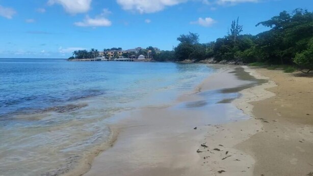A beach with clear water, a sandy shore, and a building in the background. - Donhenri House Hodges Bay in Antigua (Saint John's)