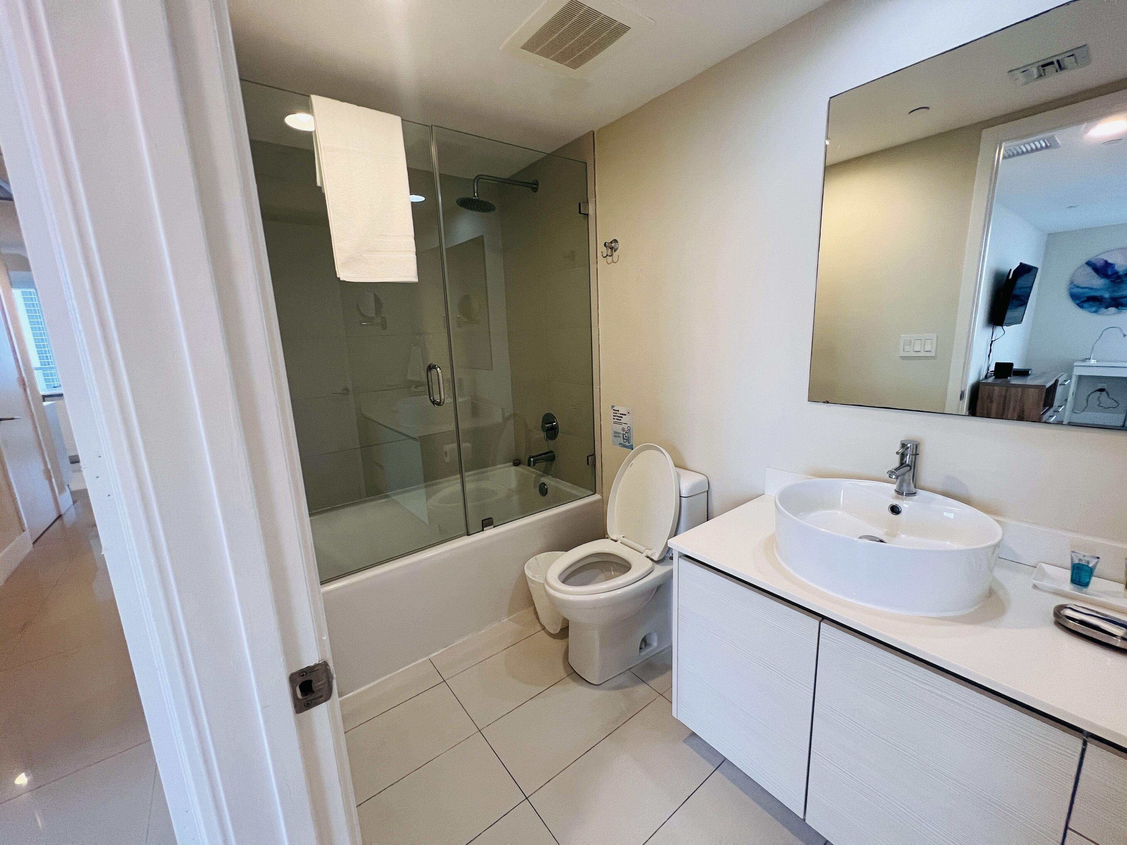 A modern bathroom with a glass-enclosed shower, a toilet, and a sink with a large mirror above it.