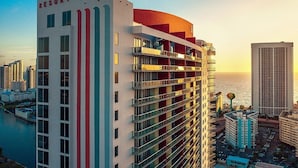 Un hôtel de grande hauteur doté de nombreux balcons, d’une enseigne bien visible indiquant « RESORT » et offrant une vue sur l’océan.