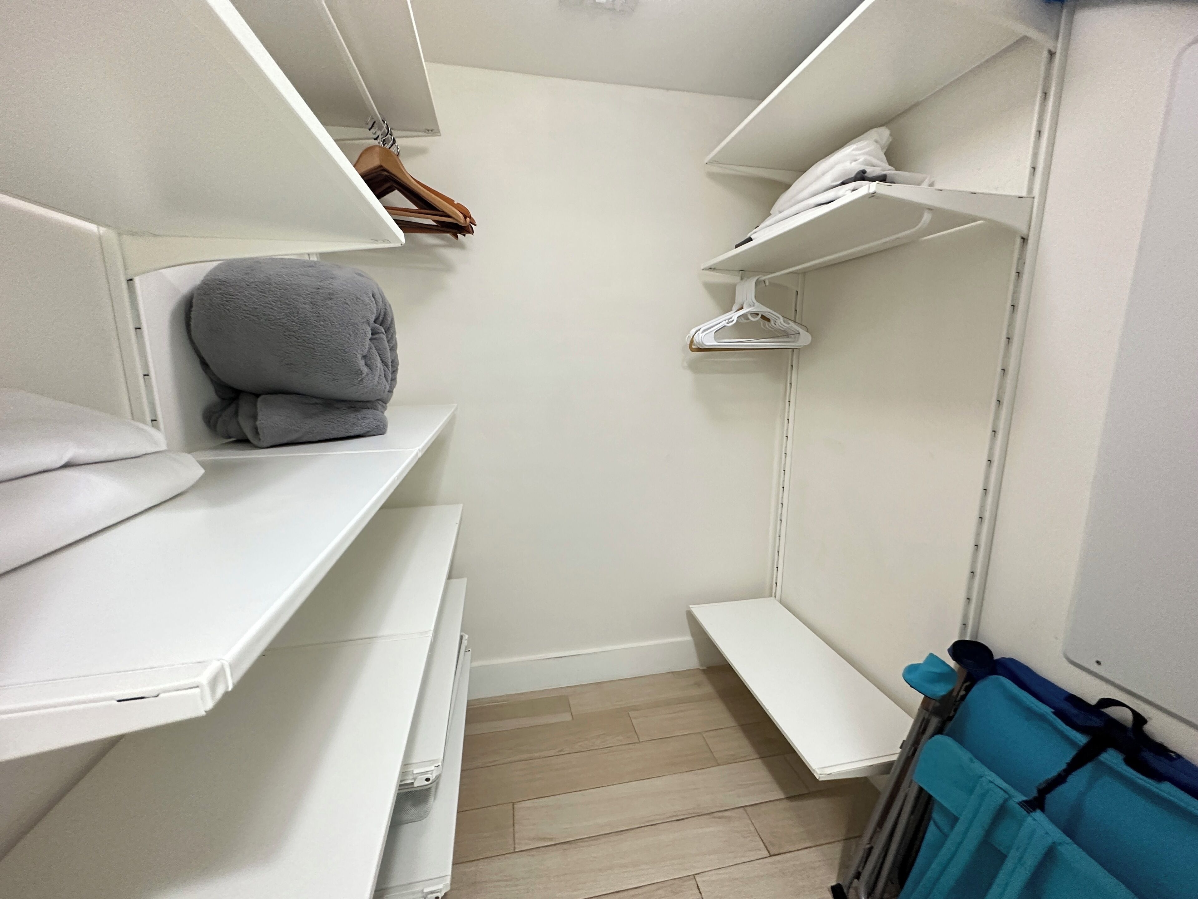 A walk-in closet with white shelves, a grey towel, and a blue bag.