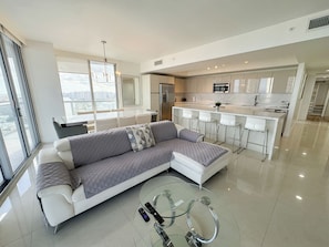 A modern living room with a sectional sofa, a glass coffee table, and a view of the city. - Beachwalk Resort (Hallandale Beach)