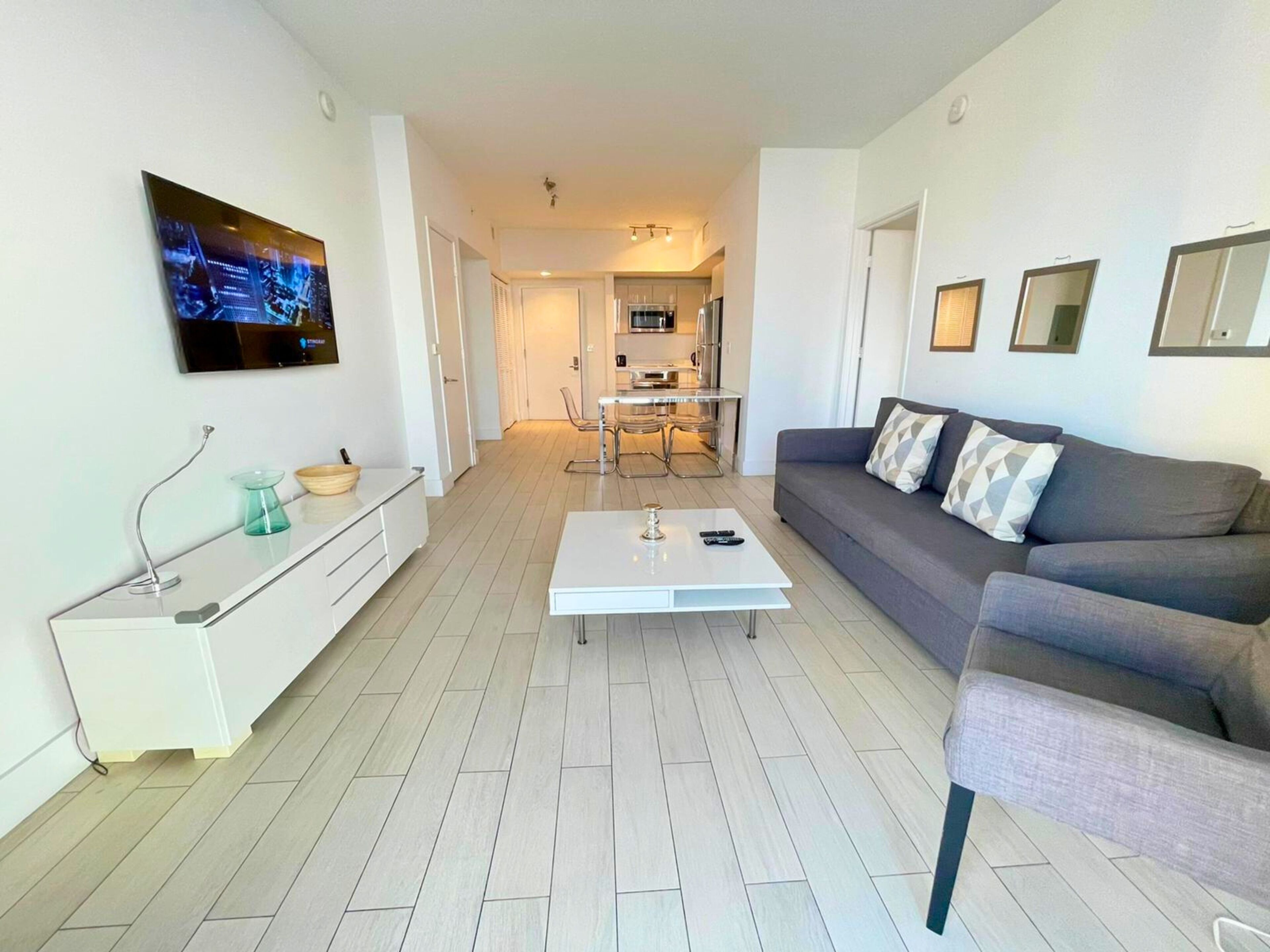 Un salon moderne avec un canapé gris, une table basse blanche et un téléviseur fixé au mur.