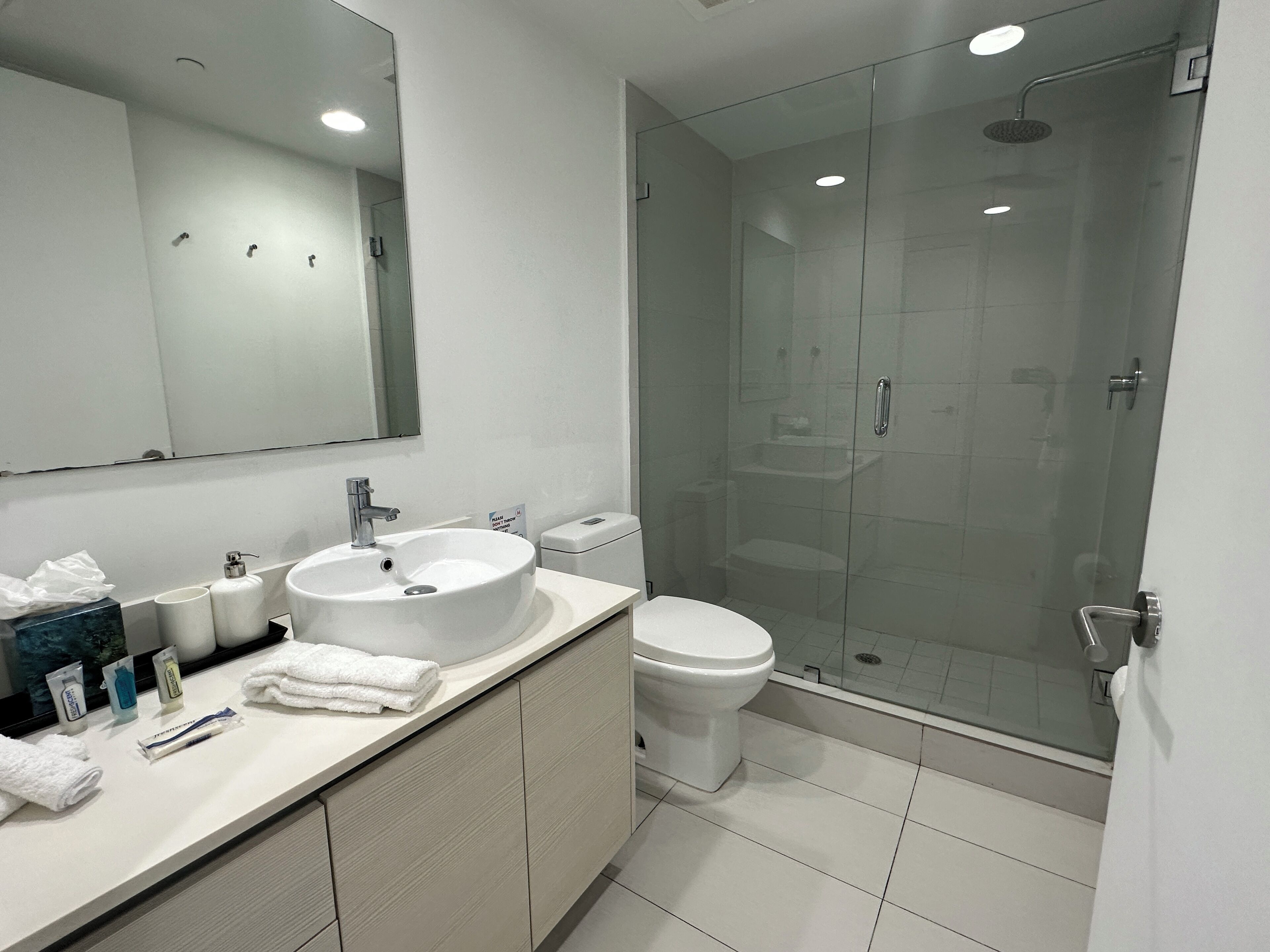 Un bagno moderno con un grande specchio, un lavandino bianco, il water e una cabina doccia in vetro.