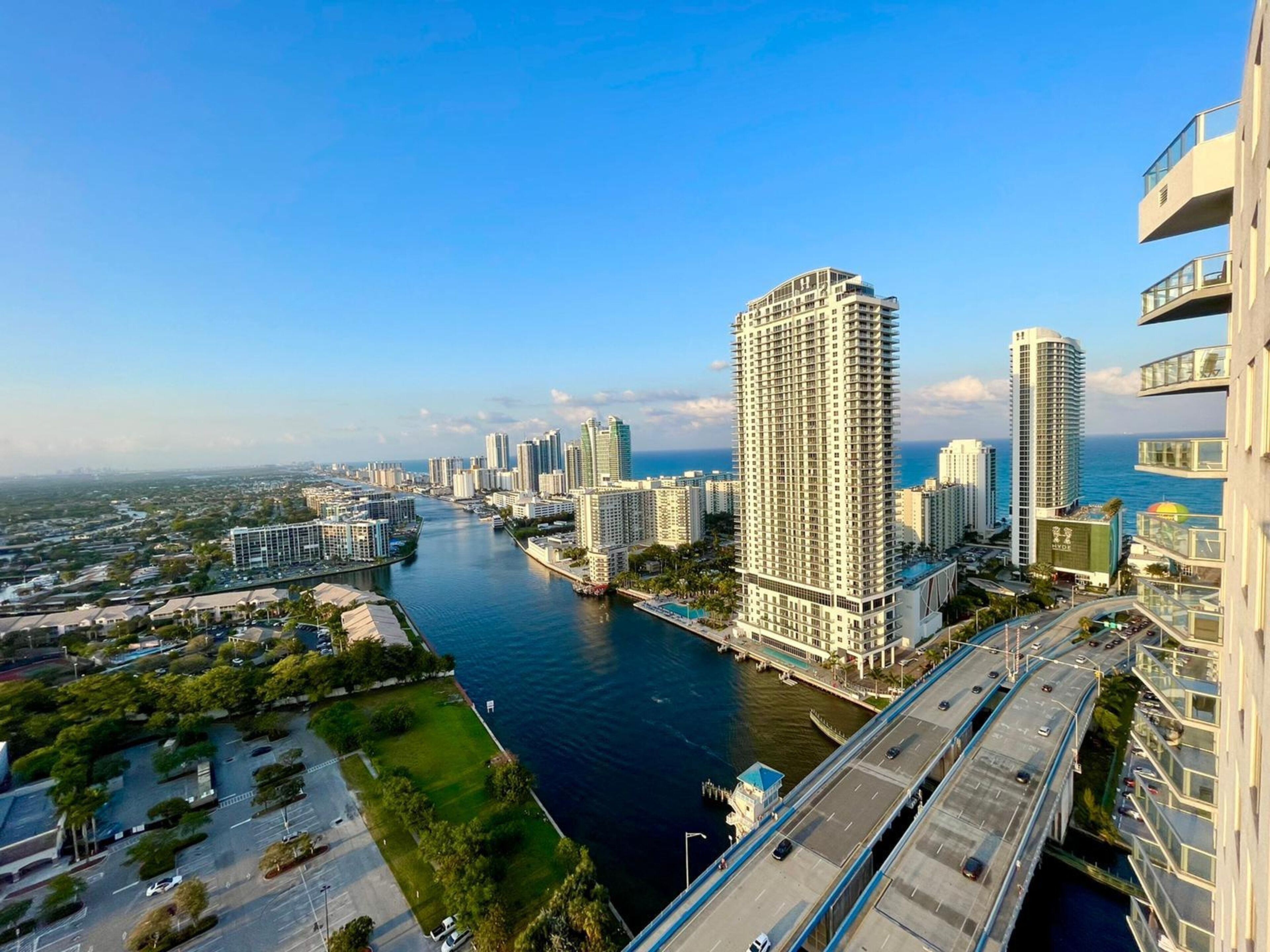 A high-rise building with a river in the foreground and a bridge in the background.