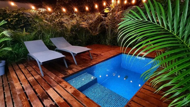 Una terraza de madera con una piscina pequeña, dos sillas de descanso y plantas en macetas.