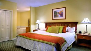 A hotel room with a large bed, two bedside lamps, a nightstand, a framed picture on the wall, and a door to the left.