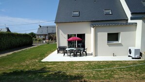 Et hus med en patio, et bord med stole og en rød parasol.