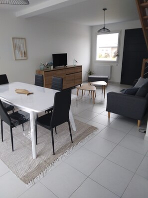 Een moderne woonkamer met een eettafel, bank en een televisie op een houten dressoir.