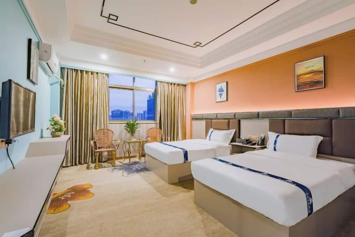 A hotel room with two beds, a desk, a chair, a TV, and a window with curtains.